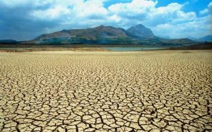 un suolo deserto con evidenti segni provocati dalla siccità e sullo sfondo montagne e cielo 